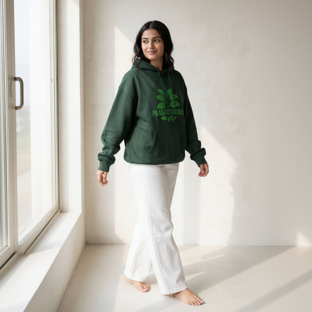 Woman wearing a green hoodie with a logo, standing in a bright room.
