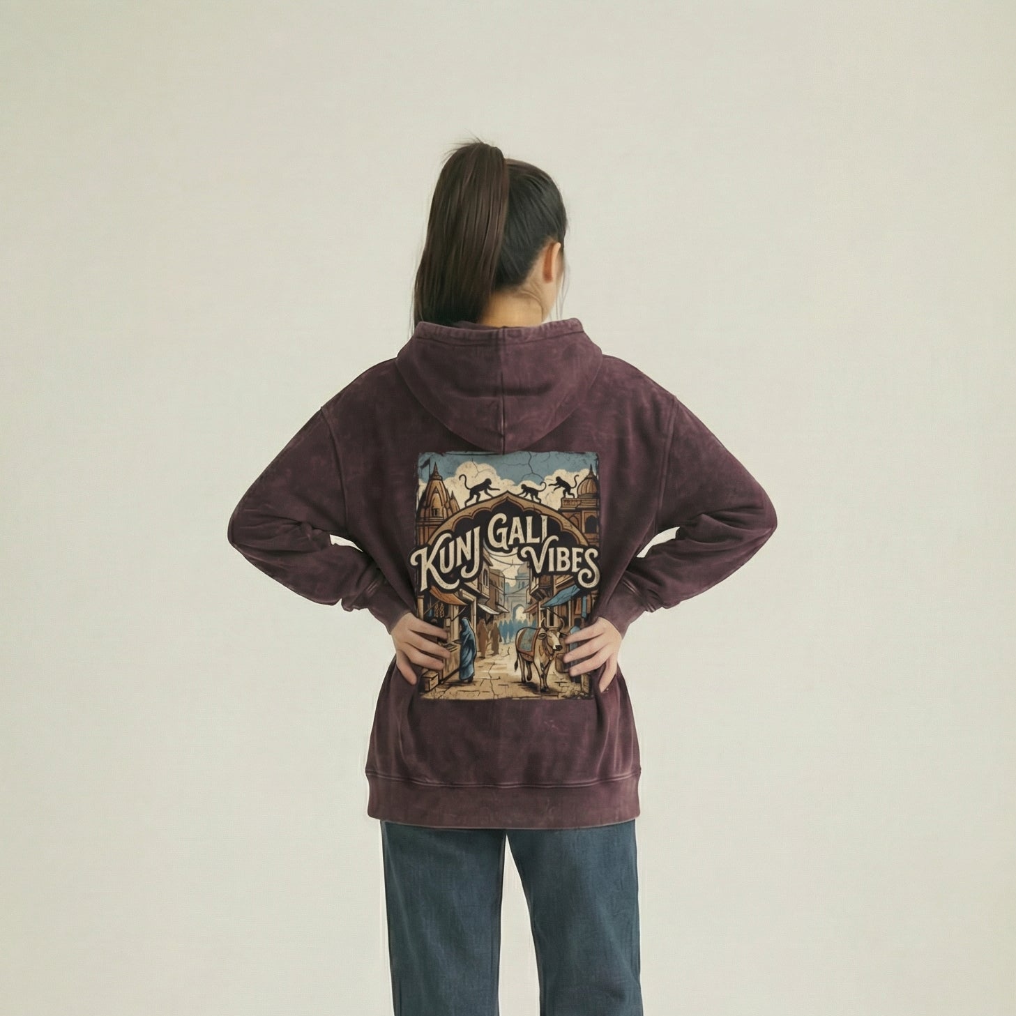 Person wearing a maroon hoodie with a graphic design on the back, standing against a plain background.
